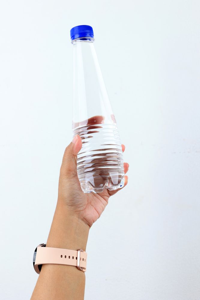 Female Hand with Pink Watch Strap Holding Mineral Water Bottle