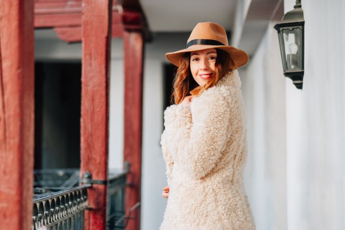 Smiling woman in warm wear standing near building and fence