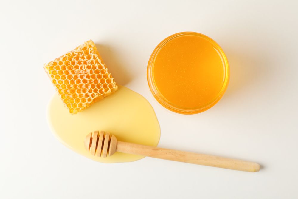 Honeycomb, dipper and jar with honey on neutral background, top view