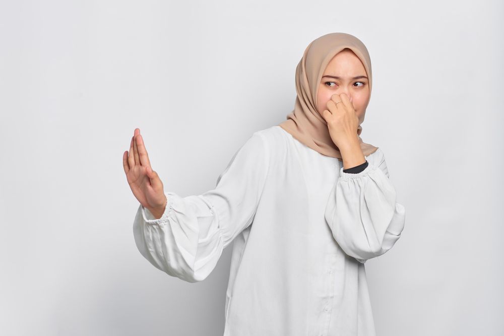 Asian female in headscarf smelling something disgusting