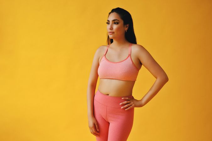 Hispanic woman in yoga clothes standing in yellow studio with one hand on hip, copy space
