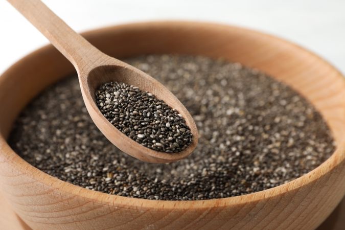 Wooden bowl with chia and spoon on wooden background, close up