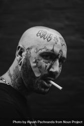 Side portrait of bald man with face tattoos smoking cigarette with band ...