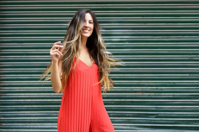 A Joyful Woman Dressed in a Vibrant Red Dress Posing Gracefully Against a Lively Green Backdrop