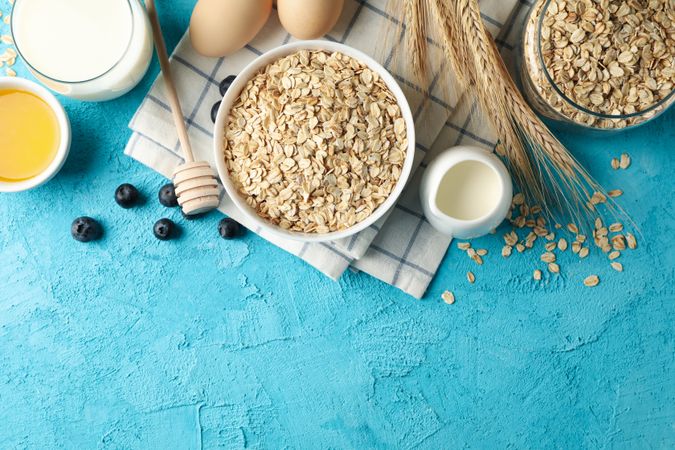 Composition with oatmeal flakes on blue background. Cooking breakfast