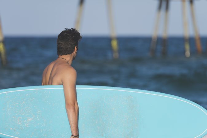 Male surfer with blue board enjoying the view of the ocean