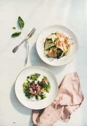 Two bowls of salad on marble table, one artichoke, one ham and pear