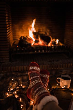 Faceless woman sitting by fireplace and holding mug
