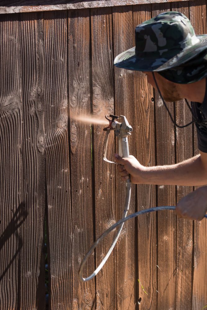 Professional Painter Spraying Yard Fence with Stain