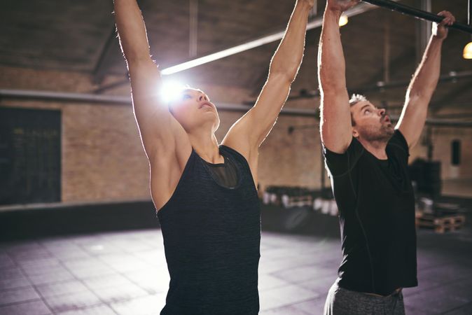 Fit woman and man with arms raised on bars preparing for exercise