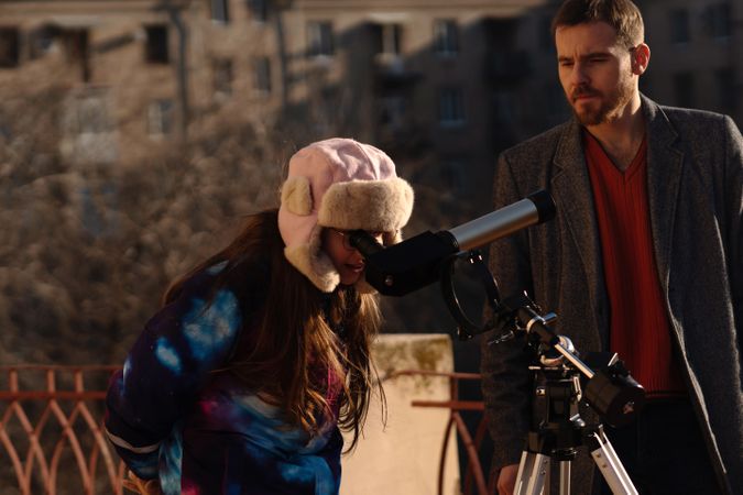 Girl and instructor use tripod-mounted telescope for rooftop solar study