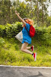 A young person with orange hair jumps happily and contentedly during a walk in a natural rural area