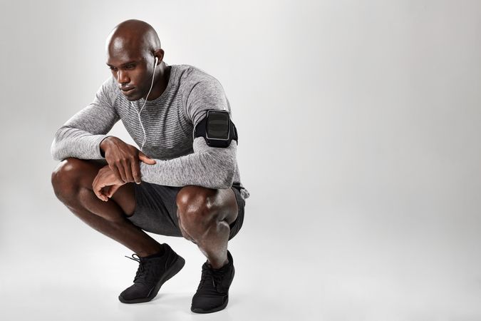 Young African male model with armband and earphone crouching down