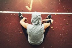 Above shot of woman in hooded vest sitting on running track