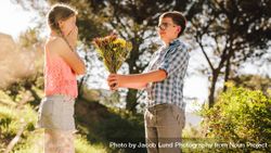 Side view of a boy proposing to his girlfriend with flowers standing in a park 4NrRr4