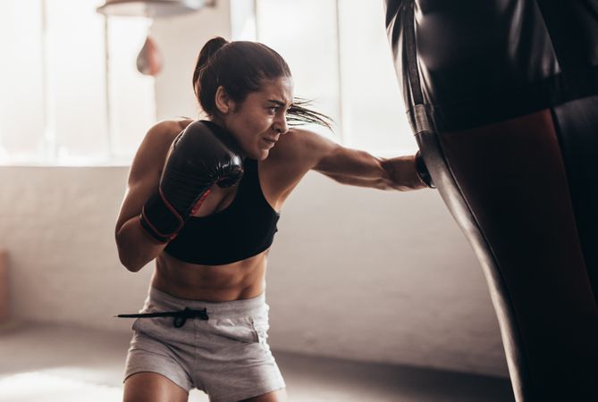Female boxer using a punching bag with gloves inside a boxing ring