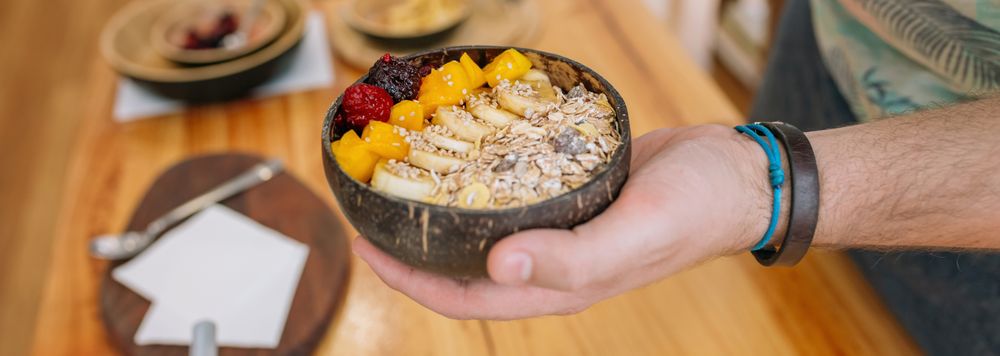 Unrecognizable chef hand showing exotic vegan fruit and cereal breakfast in coconut bowl