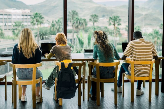 Unrecognizable young students sitting in room with laptops
