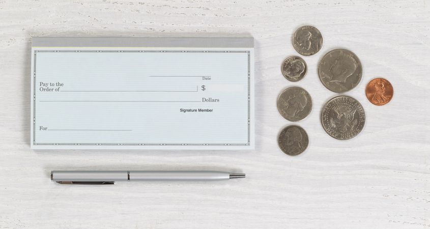 Blank checkbook with pen and coins on desktop