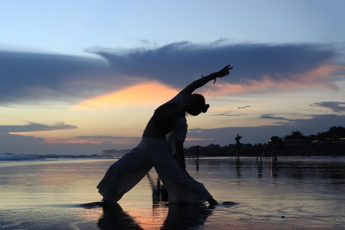 Silhouette of a woman doing yoga on water during sunset