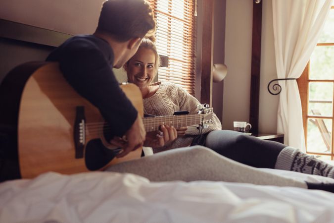 Young man playing guitar for his girlfriend in bed