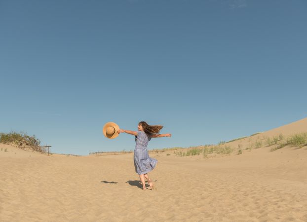 adult woman in casual dress and straw hat running having good time on sand dune