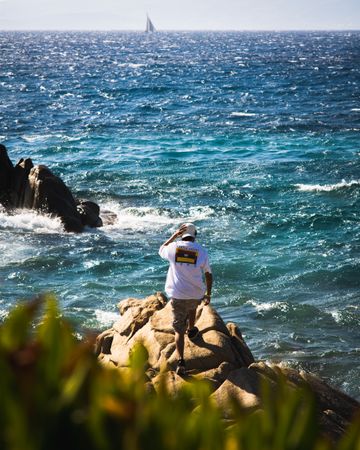 Back view of man standing on rocky seashore in Mykonos island