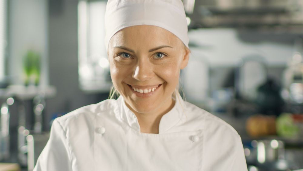 Portrait of a Young Woman Chef Smiling While Cooking in a Modern Kitchen.