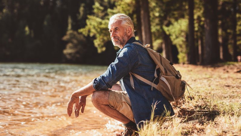 Portrait of man with backpack sitting next to a lake admiring the view