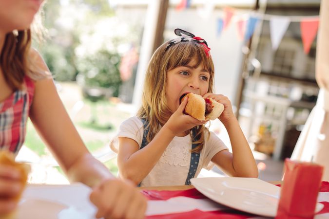 Girl eating a hot dog sitting with her family