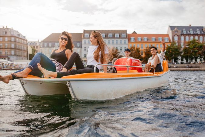 Young friends enjoying a ride on pedal boat on river with classic buildings behind