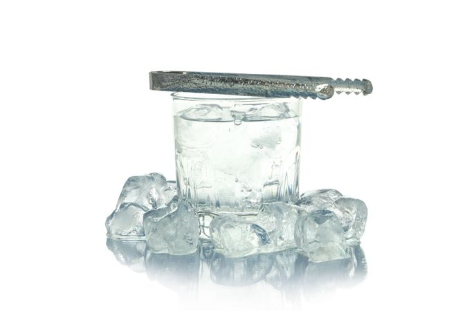 Crystal rocks glass full of water and surrounded by ice, and topped with tongs