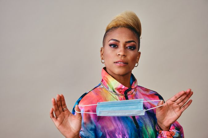 Studio shot of Black woman in bold 80s windbreaker jacket holding a face mask