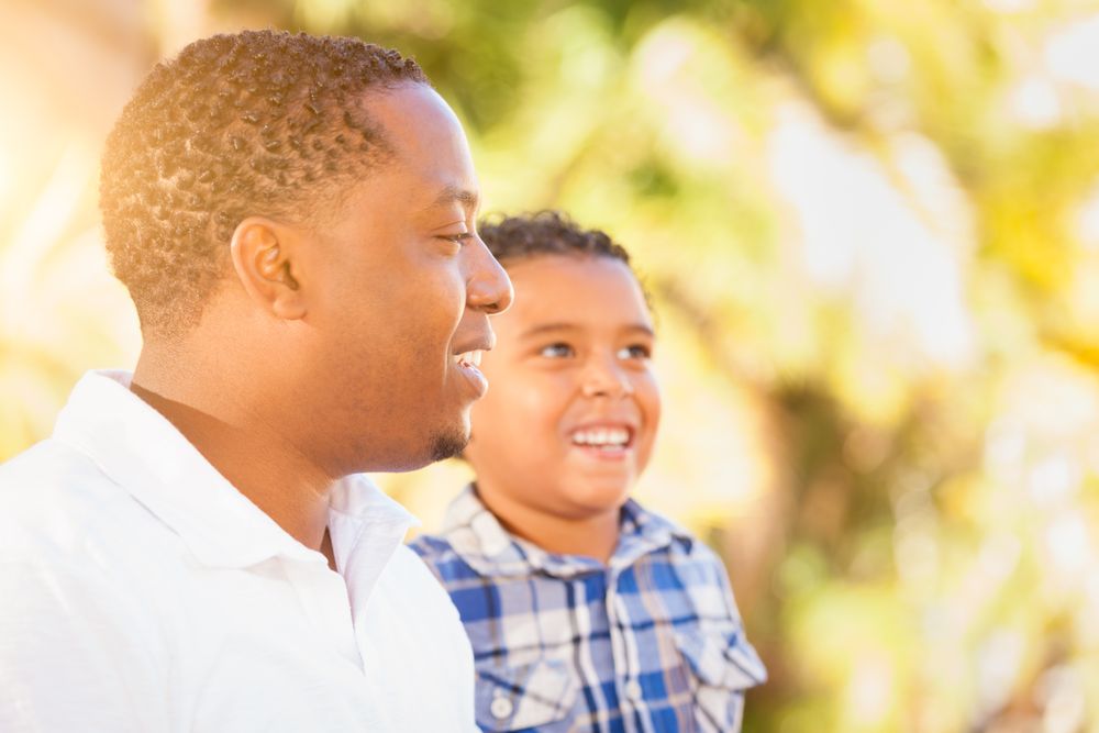 Young Black Son Sitting At Father Outdoors