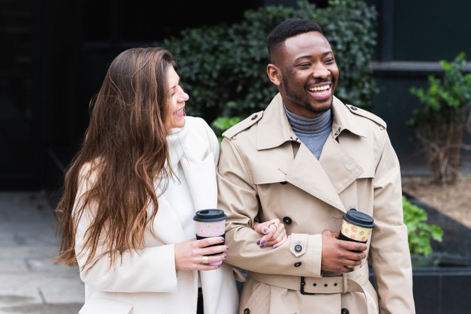 Happy multiethnic couple in stylish clothes with takeaway coffee