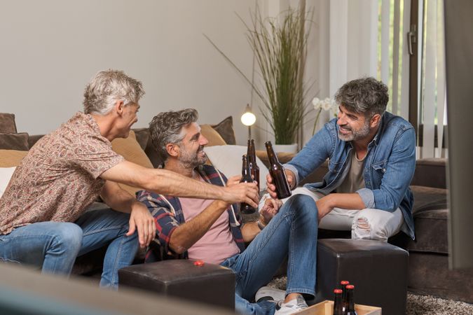 Father and mature sons clinking beer bottles and smiling at home