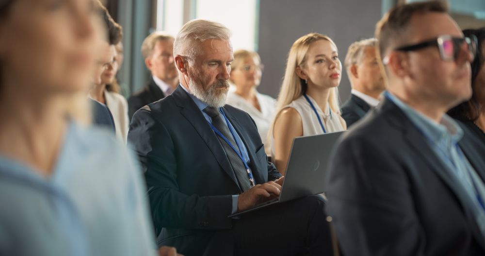Male Top Manager Sitting In Crowd And Using Laptop Computer At International Technology Conference.