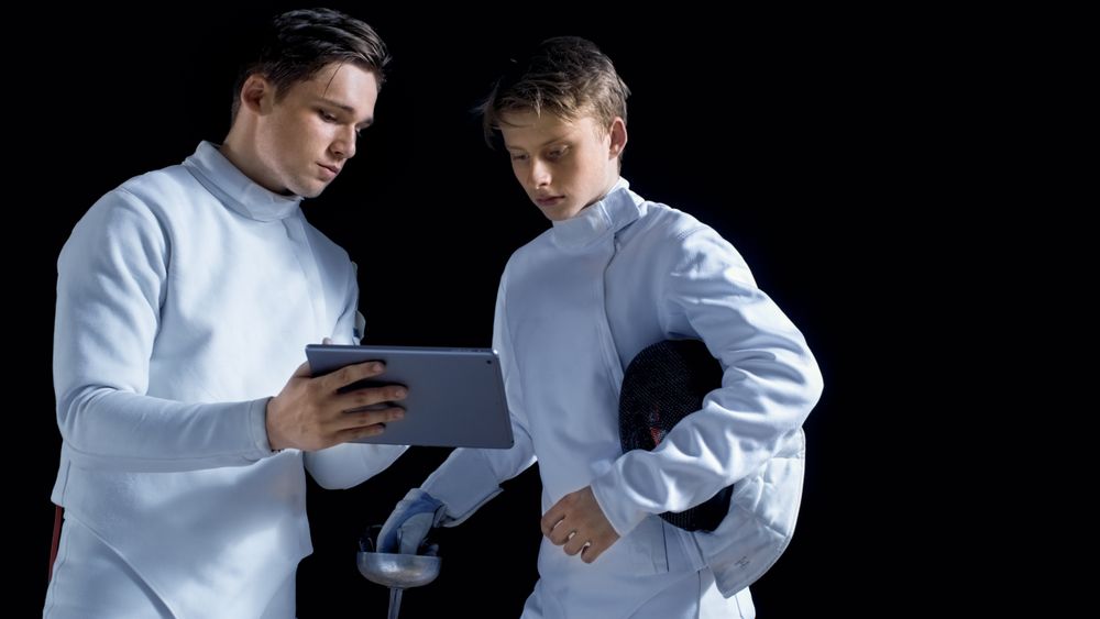Two Young Fully Equipped Fencers Use Tablet Computer To Learn More About Strategy, Attack and Defense in Fencing.