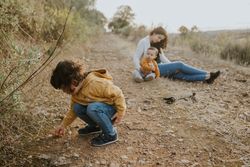 Mother sitting on walking trail outside with her baby boy and daughter exploring plants nearby