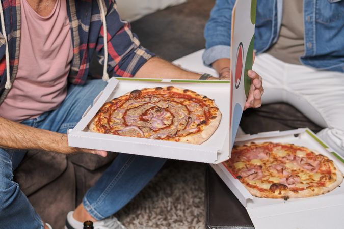 Crop men holding packages with pizza in living room