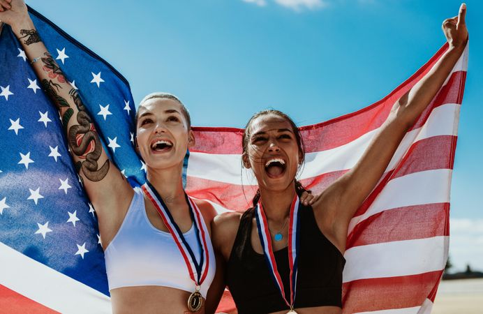 Female athletes celebrating victory holding American flag outdoors at stadium