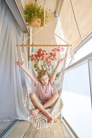 Boy sitting in hammock chair on balcony