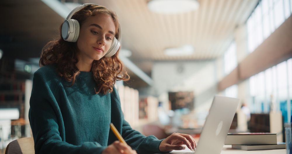 Engaged Young Female Student Studying With Headphones in Modern Library.