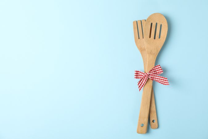 Wooden fork and kitchen spatula on blue background