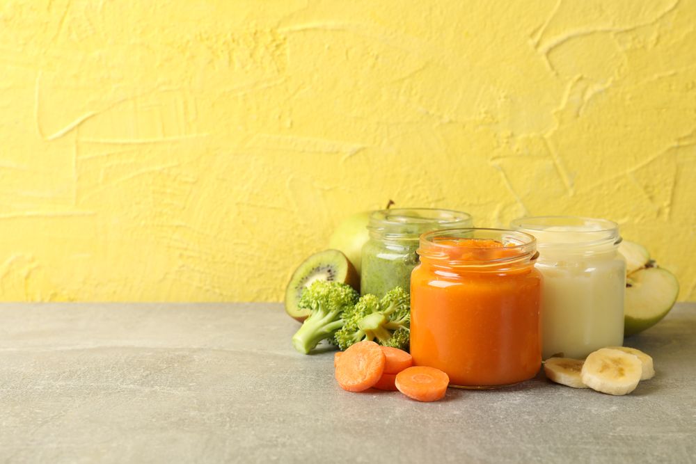 Composition with baby food on gray table against yellow background