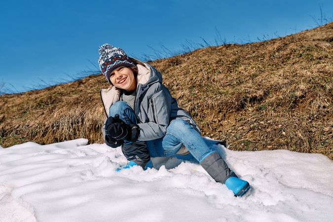 Cheerful boy making snowball in nature