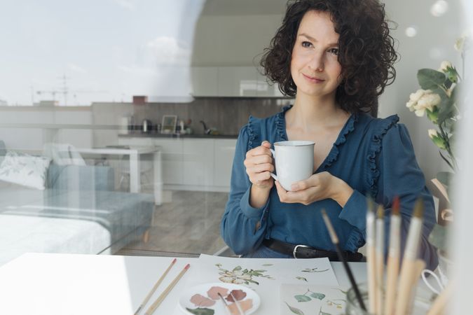 Pensive painter sitting with cup of coffee at work