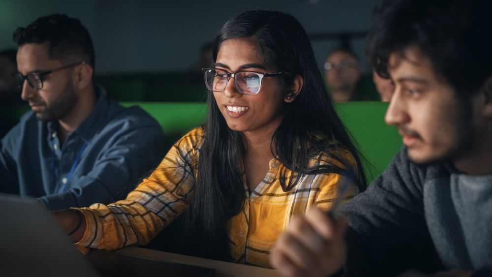 Group of Diverse Happy Students Having a Conversation in University Classroom, Working on a Shared Research Project on a Laptop Computer.