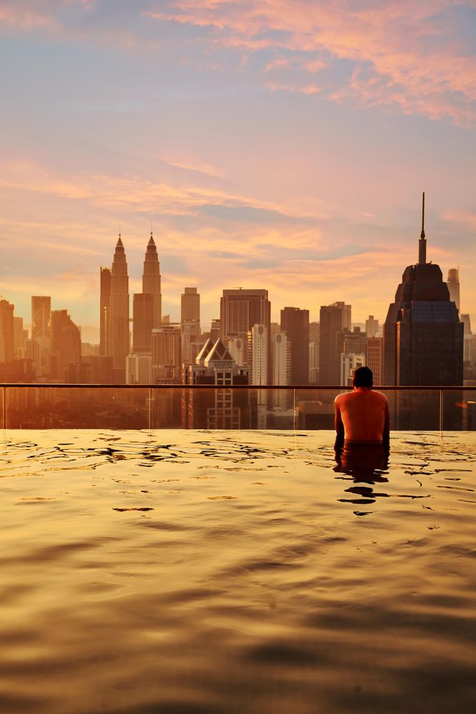Man relax in swimming pool in sunrise, enjoying city view in the morning