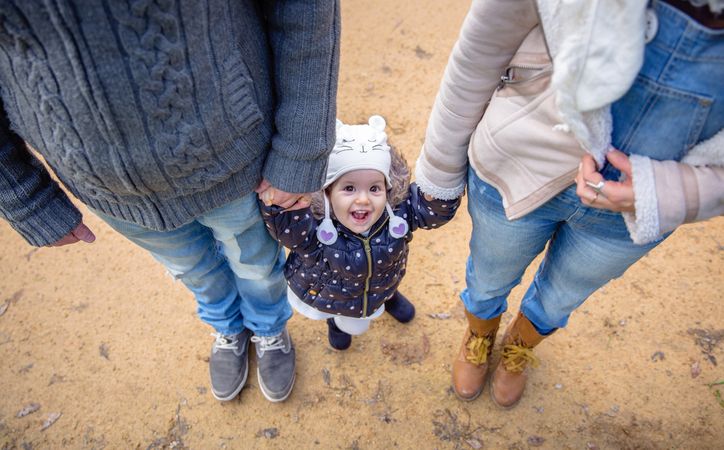 Little girl looking up while holding her parents hand outside